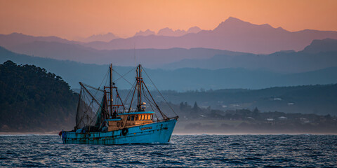 Obraz premium Fishing Trawler in Ocean with Mountain Backdrop at Sunset