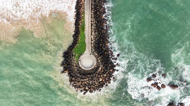 Aerial view of a stone breakwater with a circular platform surrounded by turquoise waves crashing on the shore in Galle, Southern Province, Sri Lanka.