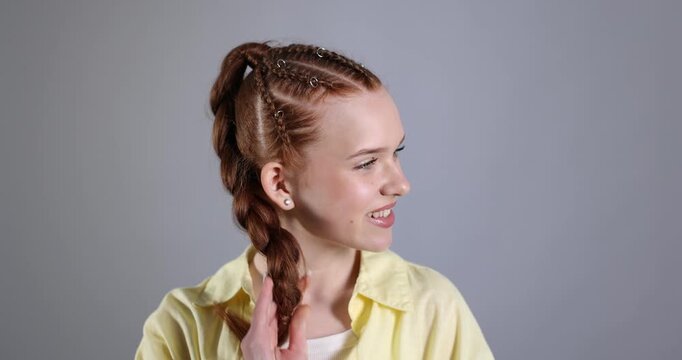 Smiling teenage girl with beautiful braids posing on grey background