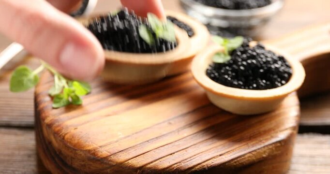 Woman taking tasty tartlet with black caviar at wooden table, closeup