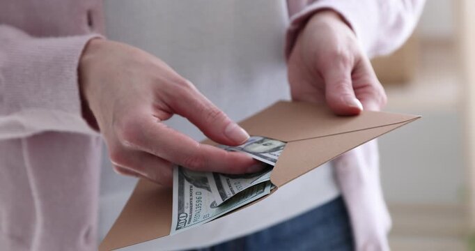 Woman opening envelope with dollar banknotes indoors, closeup