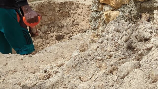 Close-up footage of a construction worker digging a septic tank pit with a shovel in sandy soil. Ideal for sanitation infrastructure, excavation, wastewater systems, and construction industry projects