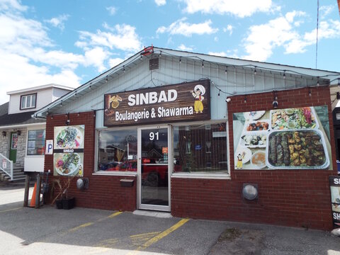 Gatineau, Quebec, Canada &ndash; May 7, 2026: The brick storefront of "Sinbad Boulangerie and Shawarma" restaurant features large food photo banners, signage, and a central glass entrance at 91 boulevard Sa