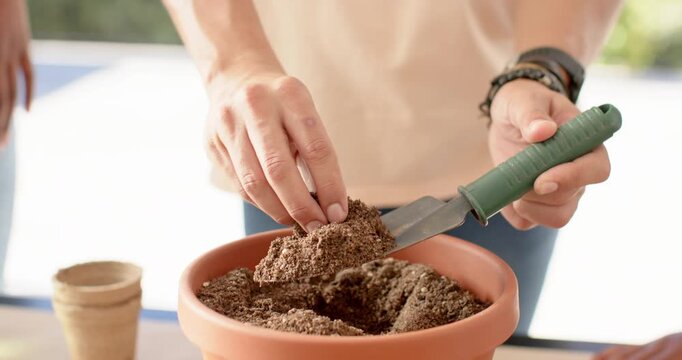 African American friends man leading scooping soil in terracotta pot planting seeds starting garden