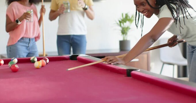 African American friends at home seeing woman aiming cue hitting ball on red-felt table, copy space