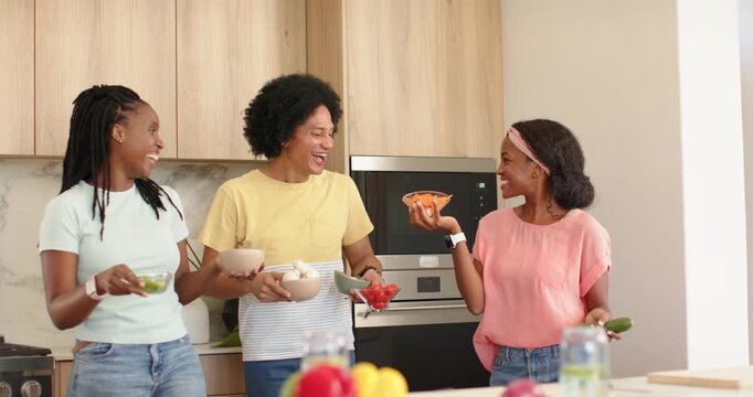 African American friends lifting carrot bowl, placing veggies on marble island, preparing salad