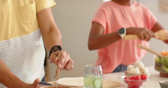 Friends starting by stirring red sauce and using wooden tongs on kitchen counter, making meal