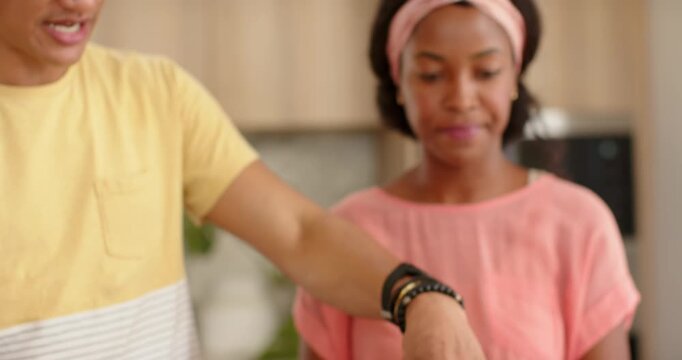 African American couple at counter with sauced crust, man adding toppings, woman grating for pizza