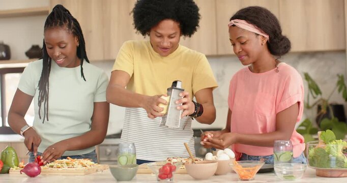Three friends chopping, grating, cracking eggs preparing dinner at kitchen counter with grater
