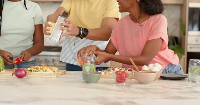 African American friends gathering at counter chopping pepper, grating on grater, assembling meal