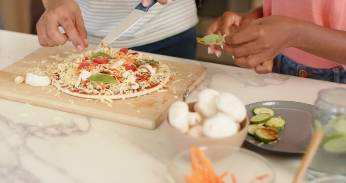 African friends assembling pizzas on counter seeing prep, nudging tomatoes with knife, using grater