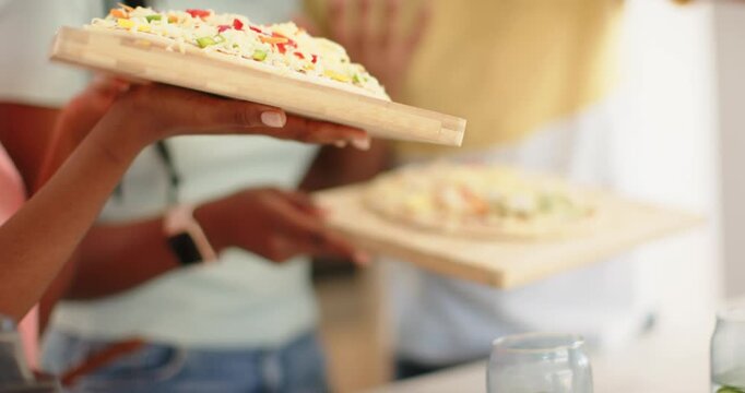 African friends comparing wooden pizza boards on counter while preparing pizzas, man seasoning