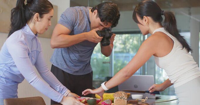 Diverse trio styling dragonfruit and avocado on board in kitchen as operator shooting DSLR closeups