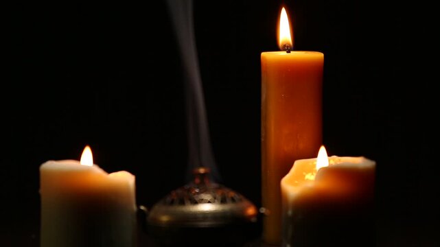 Three magic Christmas wax candle flames calm burning in home in white smoke from incense aroma stick on black dark background with copy space. Closeup yoga, spa, wellness, relaxation. No people