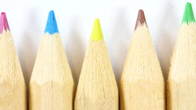 Slow pan across sharpened colored pencil tips in blue, pink, yellow, brown and green on white paper, extreme close-up of wooden art supplies with soft shadows and creative school stationery detail