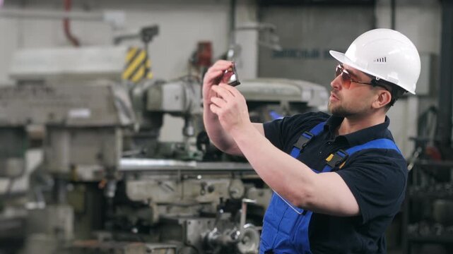 Industrial worker measuring metal part with caliper in factory workshop. Precision inspection and quality control in manufacturing environment.