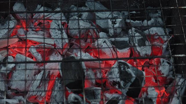 Macro glowing charcoal embers on grill, intense red heat under iron grate, ashcoated briquettes with glowing veins, textured surface, subtle smoke and crackle mood, cinematic macro detail ideal