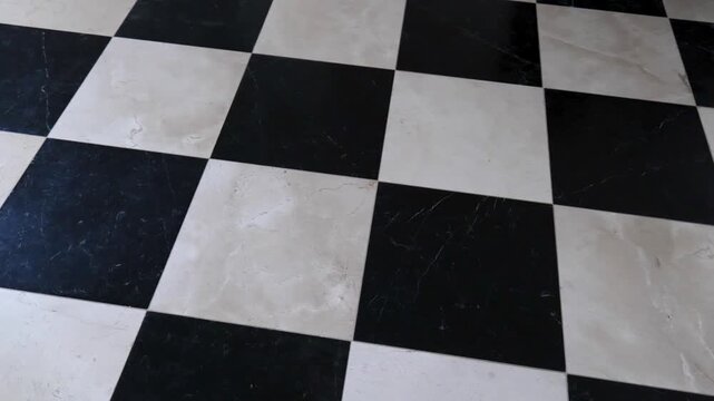 Slow pan across black and white checkered marble tile floor in an empty interior, simple geometric checkerboard pattern with polished stone texture for church, hallway or office flooring, no people