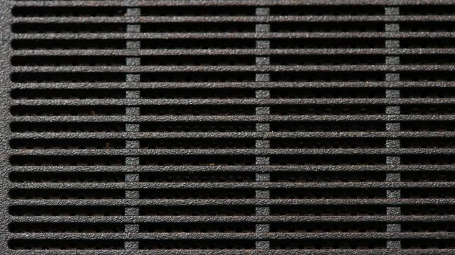 Slow macro pan across black plastic ventilation grille on textured electronic device casing, close-up of cooling air vents, horizontal slats, rough matte surface and copy space, no people