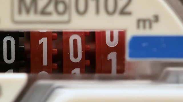 Extreme close-up video of a mechanical water meter counter rolling past 100 m3, red and black odometer digits moving behind plastic cover, utility consumption measurement and billing concept no people