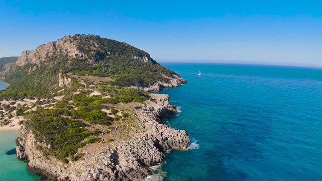 Cinematic drone flight around rocky peninsula at Voidokilia Beach in Greece, aerial Mediterranean coastline with turquoise sea and sailing yacht