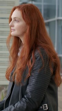 Vertical video: Closing eyes, red-haired woman in black leather jacket checking wristwatch on bench