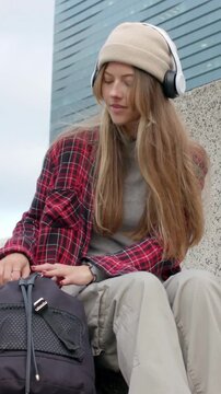 Vertical video: Reaching in pack woman in beanie and phones pulling apple on ledge checking to eat