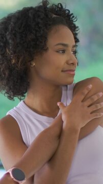 Vertical video: Centering, turning woman holding self-hug on porch, smiling, light tank, pink watch