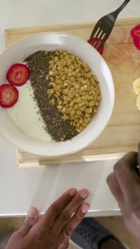 Vertical video: Picking strawberries, hands entering and arranging on yogurt at home for breakfast