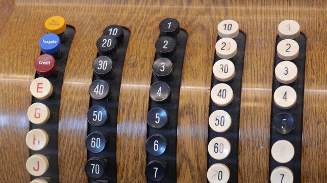 Close-up of an old fashioned cash register with round numbered buttons on a wooden panel, vintage retail accounting machine detail with black and cream keys, letters and credit button, no people
