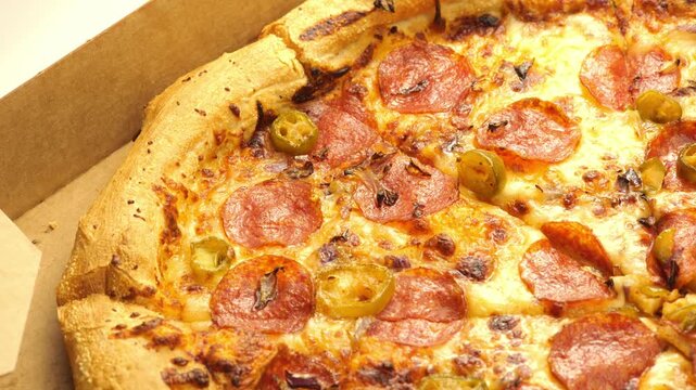 Close-up of pepperoni pizza with jalapeno slices and melted cheese inside an open cardboard delivery box, thick golden crust and baked toppings in appetizing fast food detail, no people