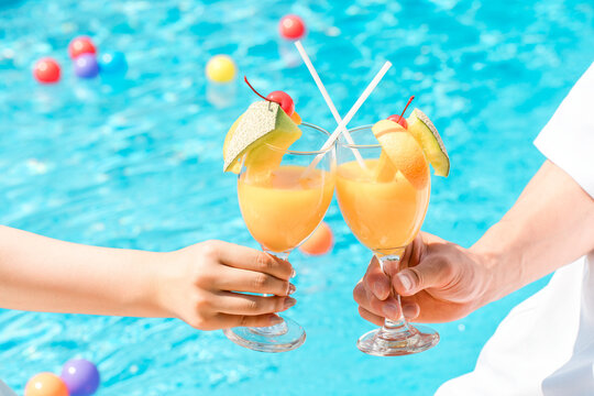 A couple toasting with tropical drinks by the poolside of a vacation resort hotel.
