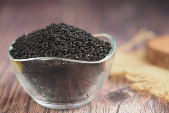 Black cumin seeds in a glass bowl on a wooden surface