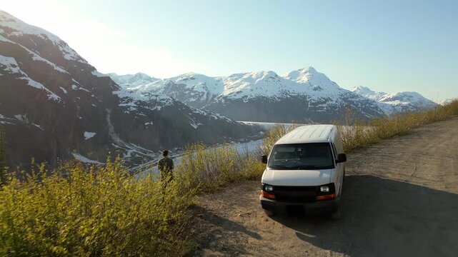 Man with camper van on a dirt road overlooking Salmon Glacier with snowy mountains in British Columbia, Canada