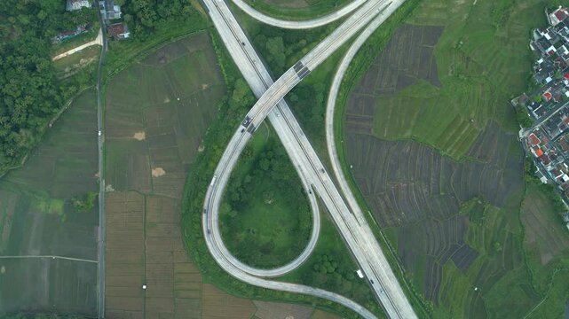 Aerial view of Bawen - Salatiga toll roads interchange with winding roads, lush green rice fields, and rural houses in Kecamatan Tengaran, Jawa Tengah, Indonesia.
