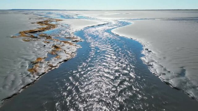 Drone perspective of a winding river flowing through a coastal mudflat on a bright sunny day