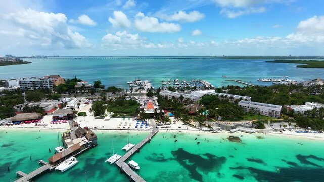 Aerial view tracking left over Playa Tortugas in Cancun, Mexico. Smooth 4K 60fps drone shot showcasing a vibrant tropical beach resort, boat docks, and the lagoon bridge horizon.