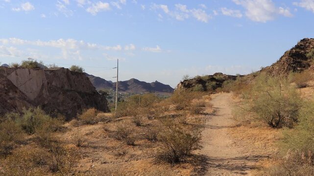 Desert trail near Tapatio cliffs, surrounded by rugged rocky hills, sparse vegetation, and expansive blue sky within North Mountain Desert Park in Phoenix, Arizona