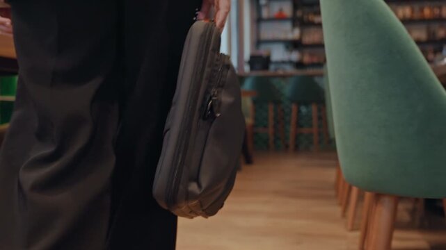 Caucasian executive walking with briefcase through cozy cafe, green chairs, wooden floor, warm lighting, business attire, steady pace, hand gripping leather bag, quiet morning commute, contemplative