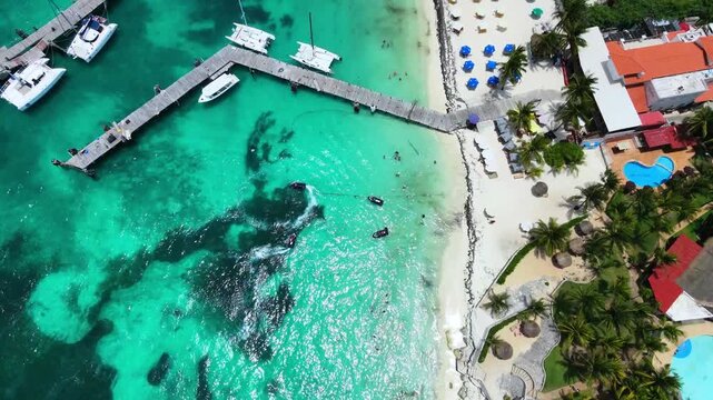 Top-down aerial view tracking the coast of Playa Tortugas in Cancun, Mexico. Smooth 4K 60fps drone top shot showcasing wooden docks, luxury catamarans, and a beach resort.
