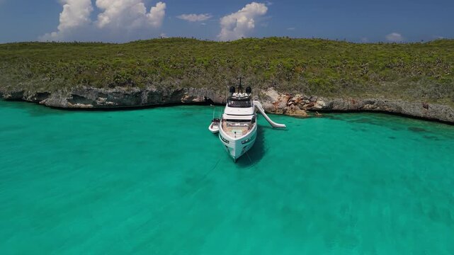 Luxury superyacht with water slide by island cliff, aerial orbit