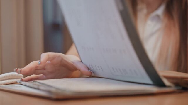 Student flipping through leather folder. Focused woman studying in cozy cafe environment. Female student flipping through pages of leather portfolio at table in peaceful cafe setting