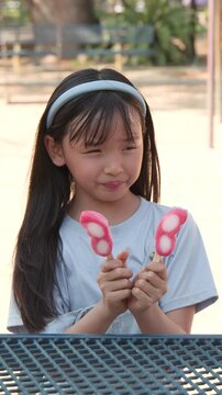 Young Asian Girl Enjoying Pink Butterfly Popsicles in Sunny Outdoor Park