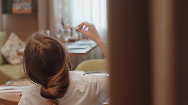 Woman at cafe adjusting messy bun while waiting at table, bistro setting with glass reflection and curtain light, switching between updo and loose hair, thoughtful pause and casual vibe