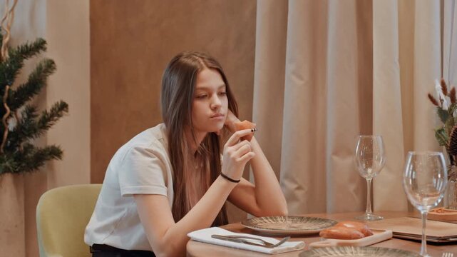 Young woman waiting alone at table, blogger checking phone with restless chin on hand, pastry untouched on plate, neutral interior tones and empty glasses, subtle tension and cinematic bokeh