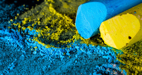 Blue and yellow chalk sticks macro closeup with colorful chalk dust powder scattered on dark blackboard art and creativity concept. © Favio