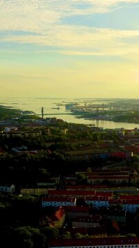 Vertical video. Gothenburg, Sweden. Panoramic Drone footage over red-roofed cityscape along the Gota Alv river at golden hour sunset, with the Alvsborg bridge and harbor district visible in the dista
