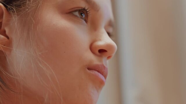 Young woman looking upward hopeful gaze, close portrait showing soft sunlight on skin, slight ear piercing visible, quiet moment of aspiration and wonder, natural tones and shallow focus evoke dreamy