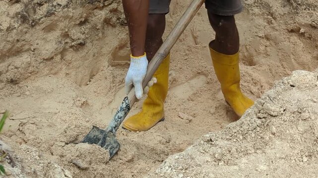Close-up footage of a construction worker digging white sand with a pickaxe at a building site. Ideal for construction materials, manual labor, excavation, and infrastructure development concepts.