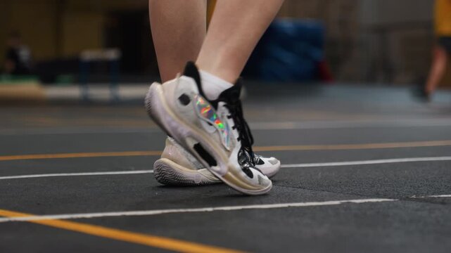 Badminton agility training court closeup rapid lateral hops, sneaker sole gripping surface, court markings, dynamic weight transfer, coach nearby, gym lighting, explosive tempo, competitive intensity
